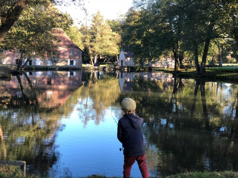 Enfant à capuche bleu marine et pantalon rouge, canne à la main au bord de l'étang du Moulin