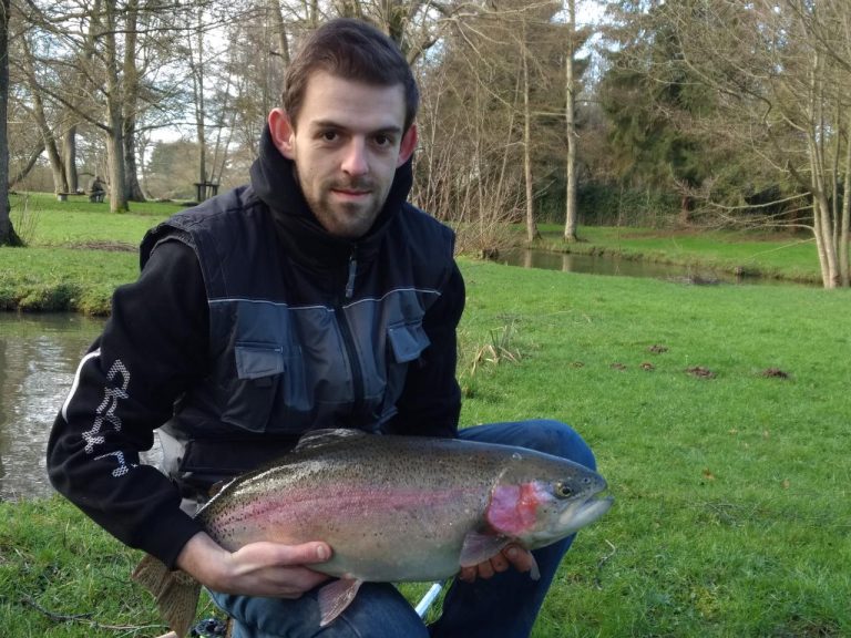 Pêcheur en veste sombre tenant une truite arc-en-ciel au bord de l'étang