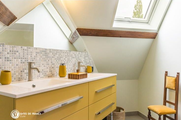 Salle de bain sous les combles : vasque allongée à deux robinets sur un meuble jaune, crédence en mosaïque