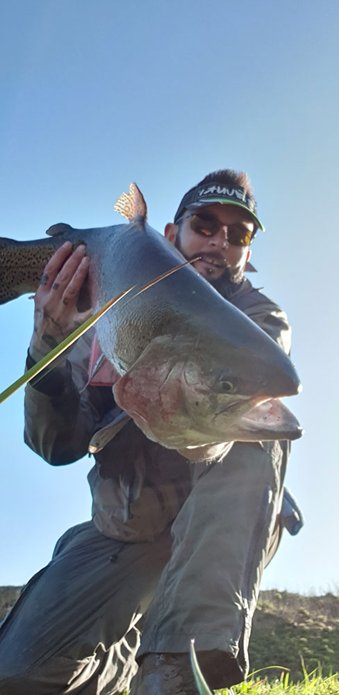 Pêcheur en casquette tenant une grosse truite arc-en-ciel sous un ciel bleu