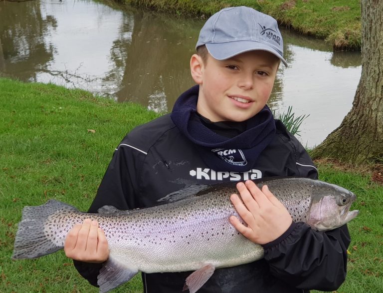 Jeune pêcheur en casquette tenant une grosse truite arc-en-ciel au bord de la rivière