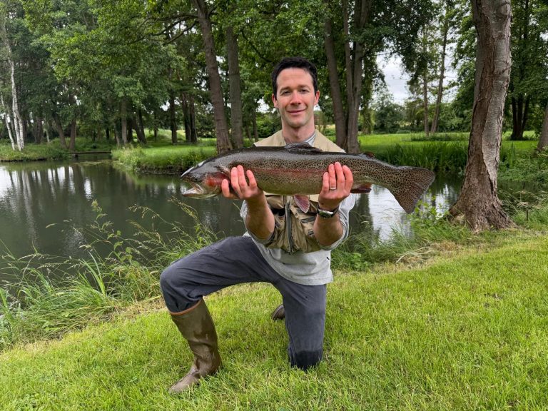 Pêcheur agenouillé au bord de l'étang du Moulin avec une grosse truite
