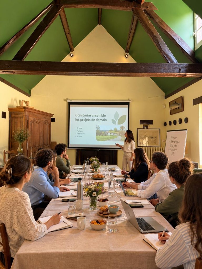 Séminaire d'entreprise au Moulin : participants installés autour d'une longue table sous la charpente apparente, face à une présentation projetée