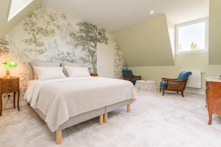 Chambre Murmure de feuilles : lit double sous les combles, devant un papier peint panoramique aux motifs d'arbres