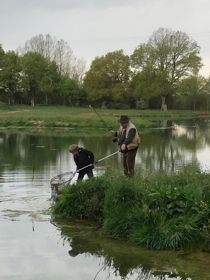 Deux pêcheurs au bord de l'étang, l'un épuisette une truite