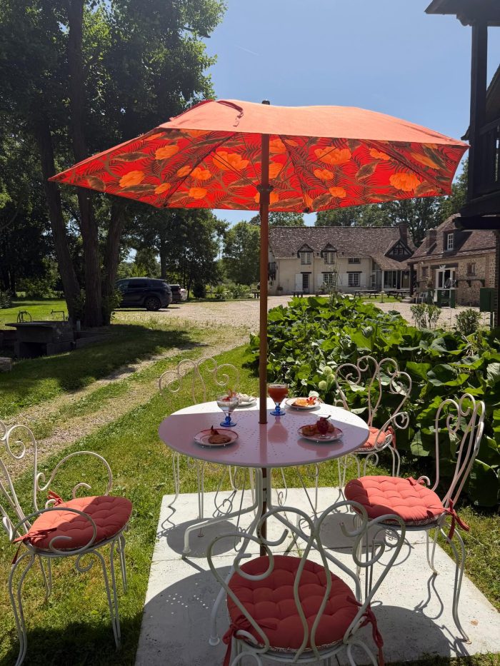 Table de jardin sous un parasol rouge devant le bâtiment du domaine